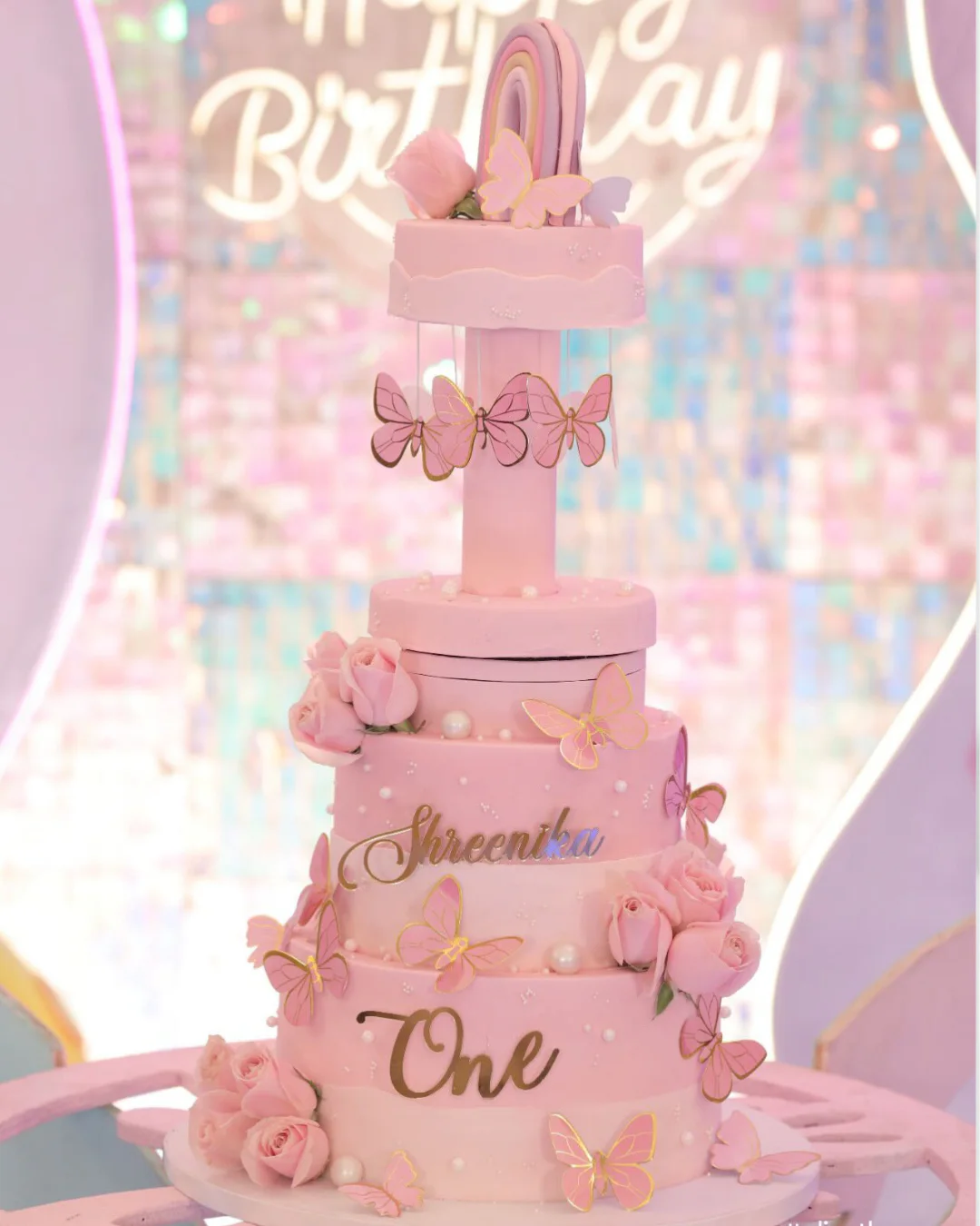 Tall pink butterfly first birthday cake with floral decorations