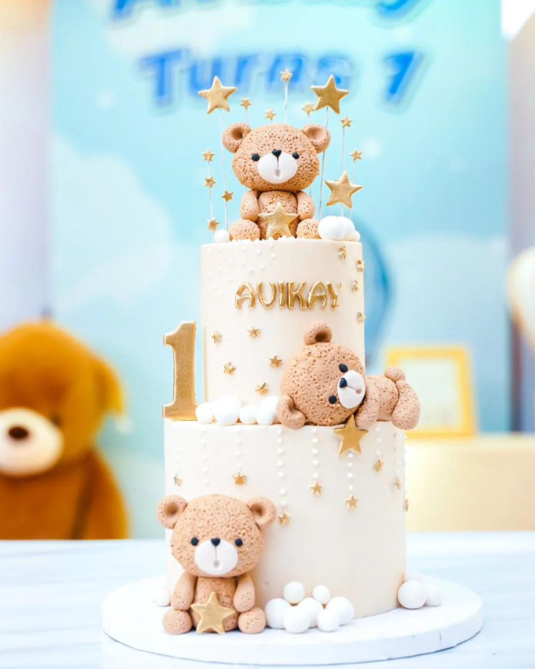 White and blue teddy bear first birthday cake with gold stars