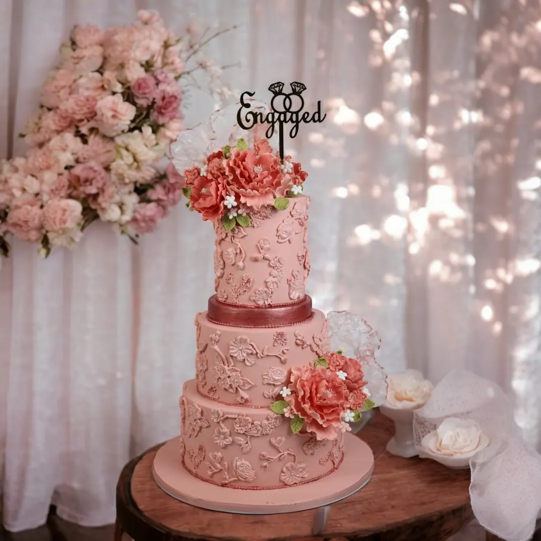 Pink tiered cake with florals and engaged topper