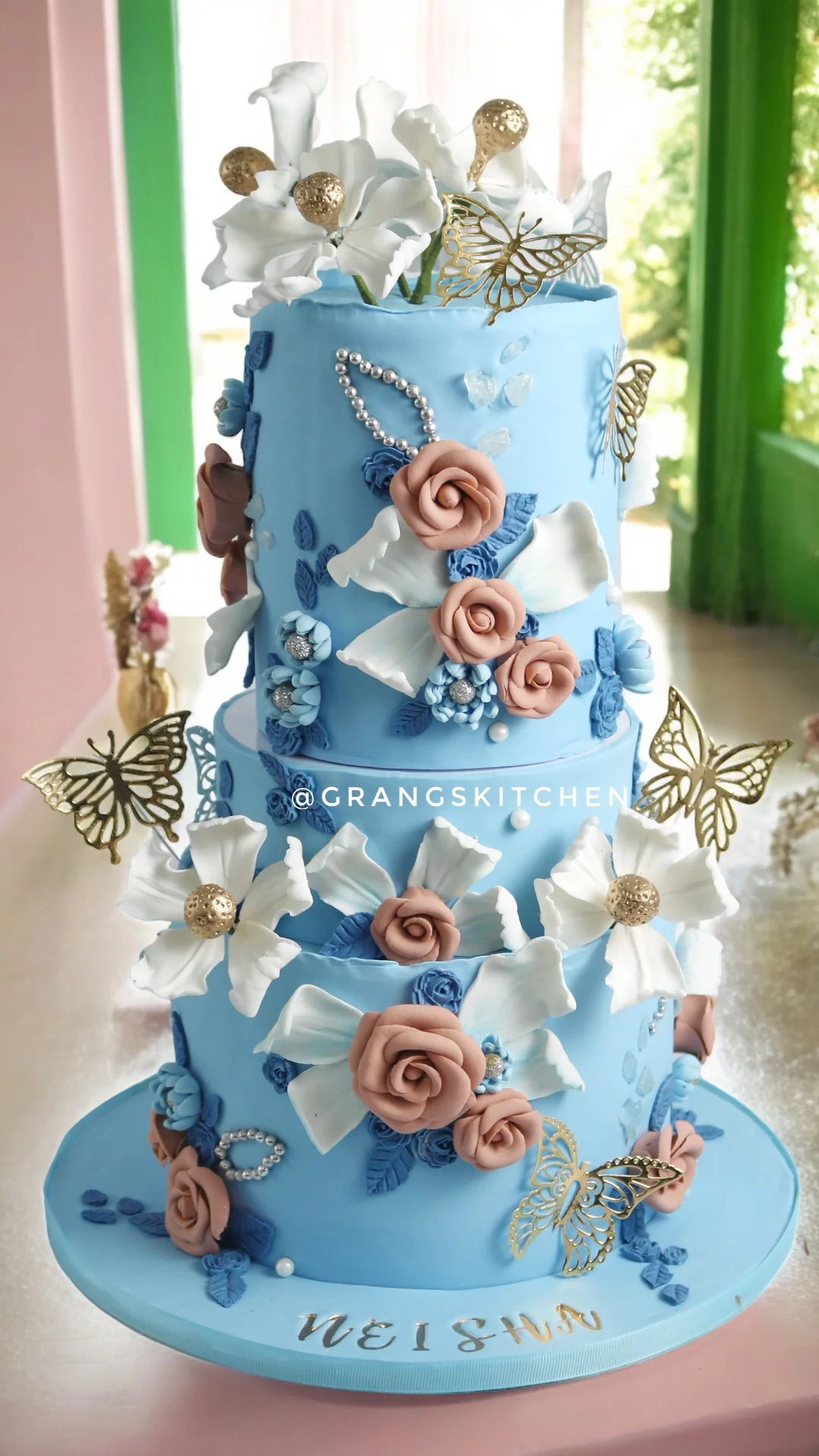 Blue three-tier wedding cake with flowers and gold butterfly details